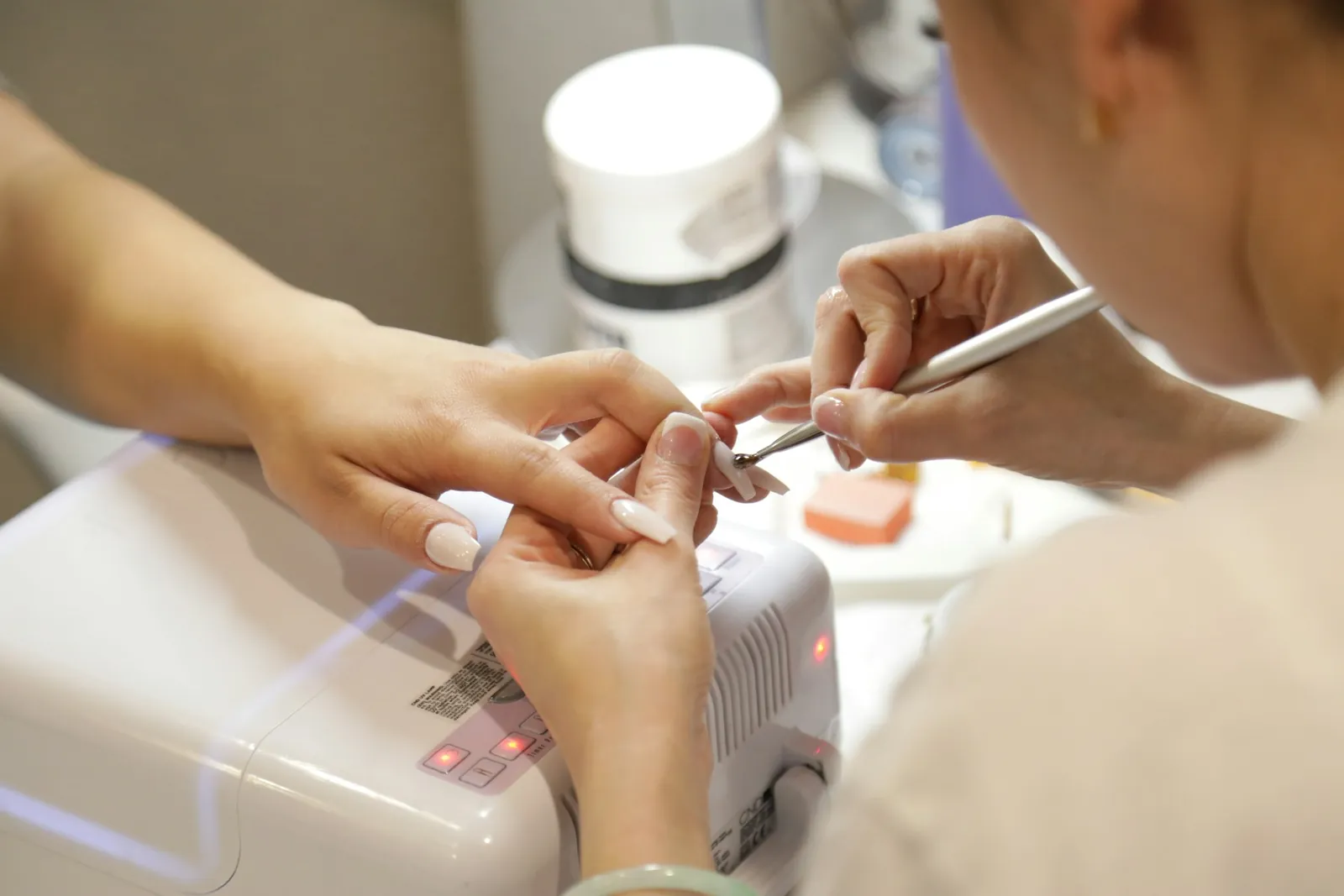 Manicure in progress at a nail salon table with a curing lamp